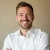 Professional male supply chain manager in business casual attire, smiling in a logistics warehouse with LED lighting – R. Simpson testimonial