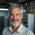 Experienced older male electrician with gray hair, standing in front of an industrial warehouse with LED lights – Walter Bumgarner testimonial