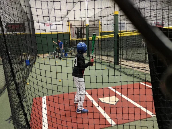 Youth baseball player practicing hitting inside indoor training facility batting cage