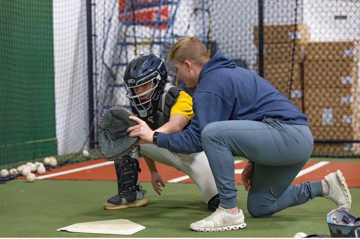Baseball coach working with youth catcher on fielding technique inside indoor training facility