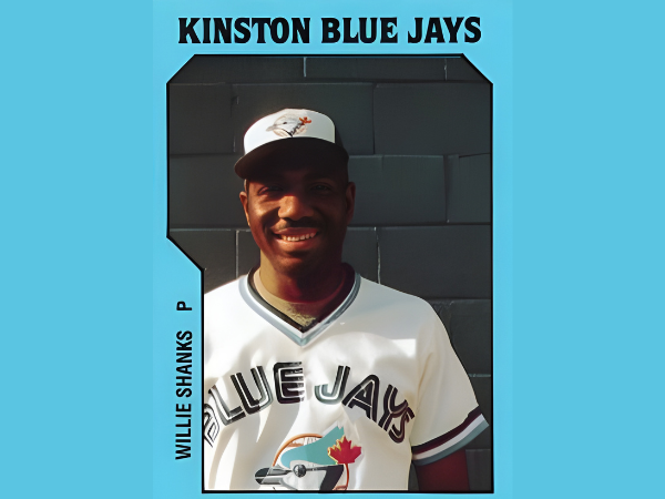 Baseball player in a Blue Jays uniform standing in front of a team backdrop