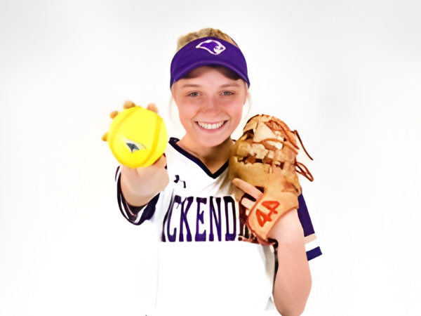 Softball player smiling and holding a ball and glove ready to train