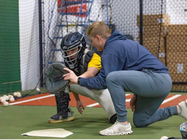 Instructor coaching a catcher during a baseball training drill indoors