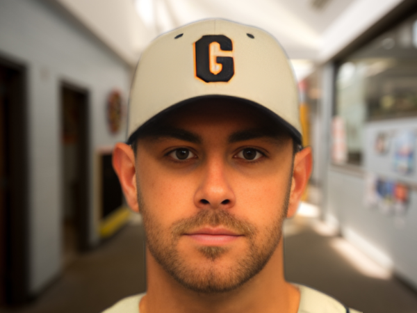 Instructor wearing a baseball cap standing indoors in a hallway