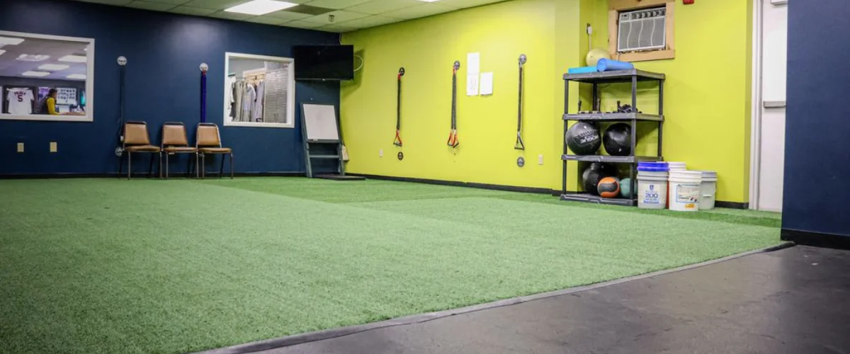 An interior view of a fitness facility with blue and lime green walls, green turf flooring, and workout equipment.