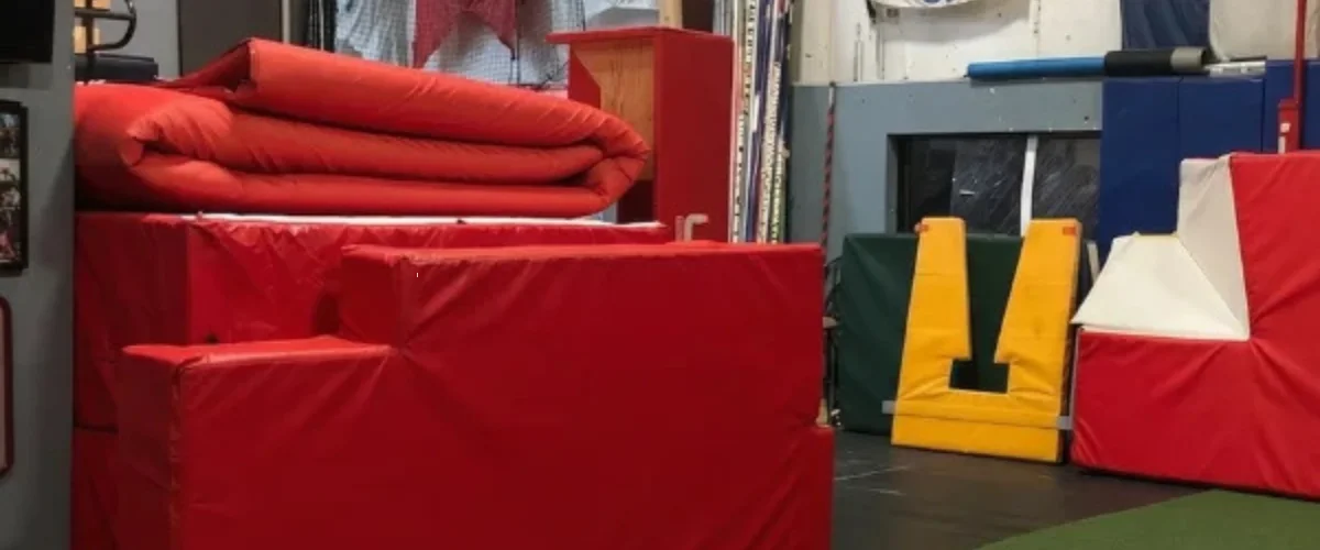 A gym with various red padded mats and obstacles, including a rolled mat and square blocks, along with elements like a yellow prop and white corner pad.