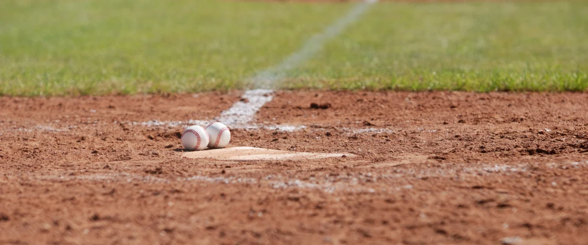 Two pristine white baseballs resting on a brown dirt infield with bright white chalk lines, green outfield grass in background.
