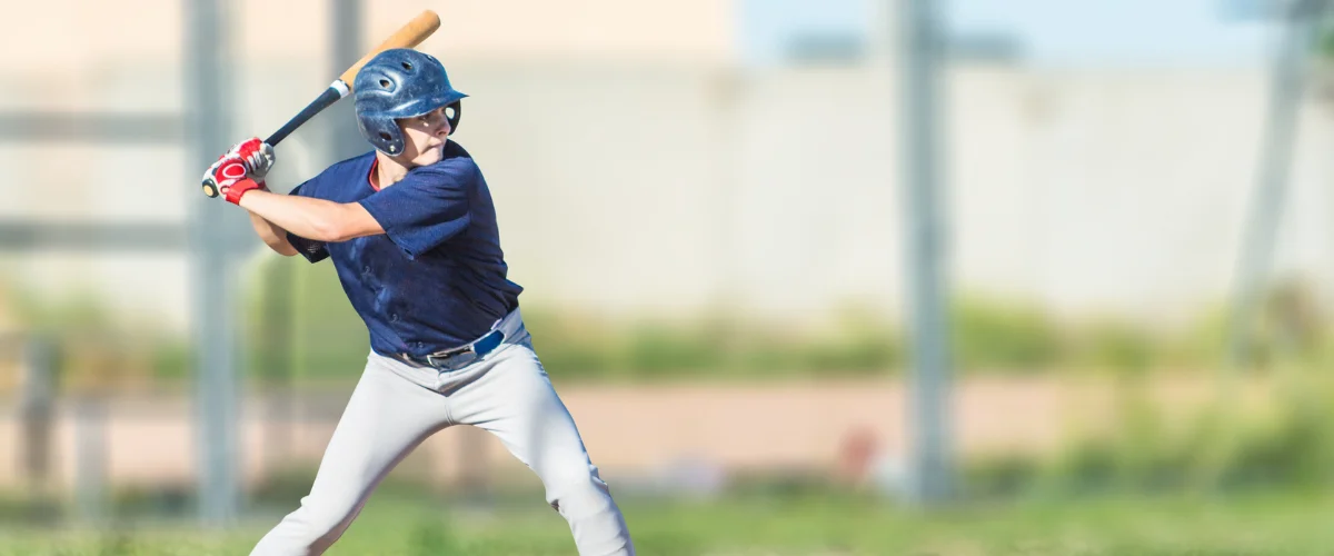 A young baseball player in a blue uniform and helmet, holding a bat in a batting stance on a sunny field.