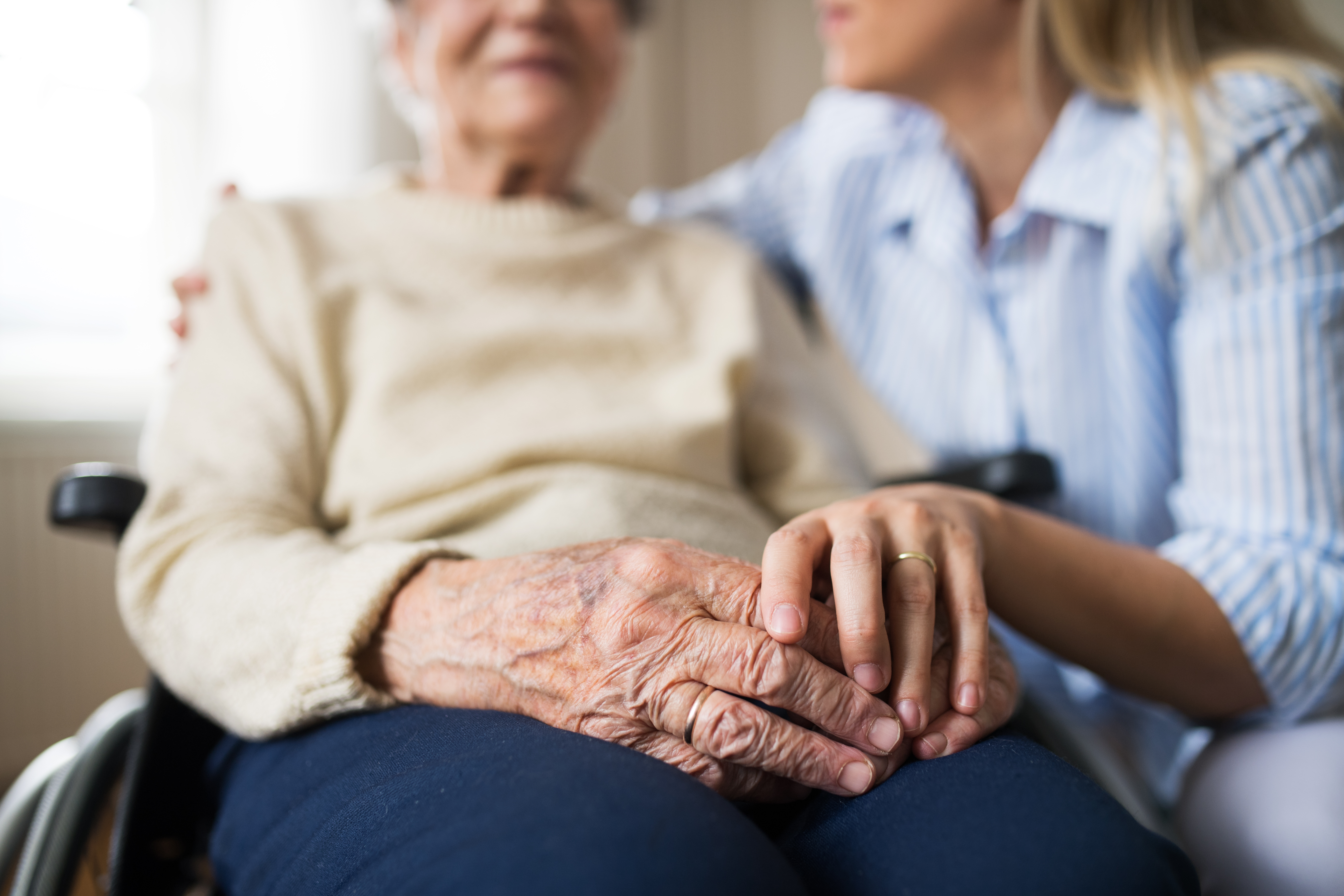 A carer holding the hand of an older person at home
