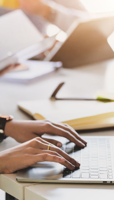 Stock photo of a woman's hands on a laptop sitting on a bed, symbolizing a relaxed approach to starting a strategy session to simplify business tech.