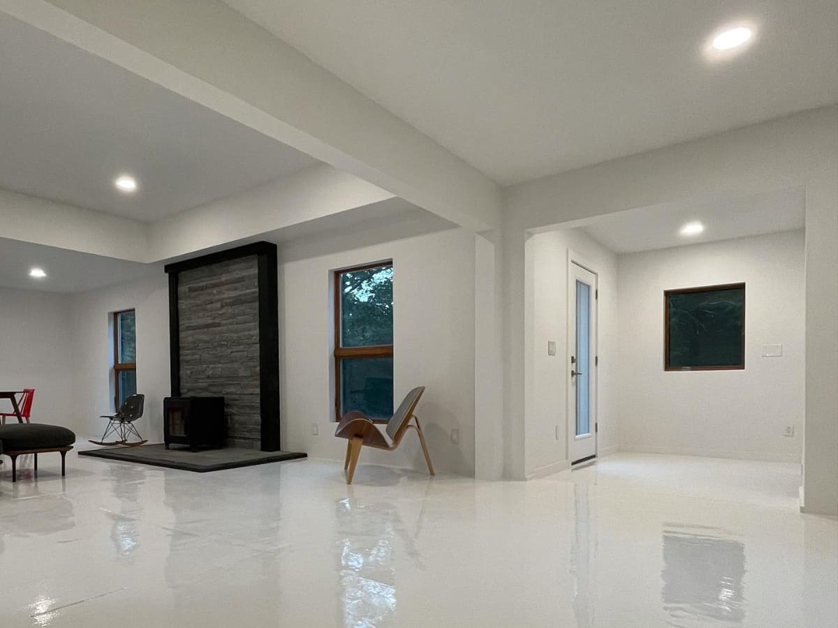 Newly built living room with white walls, large windows, a stone fireplace, and simple modern furniture in a home located in Catskill.