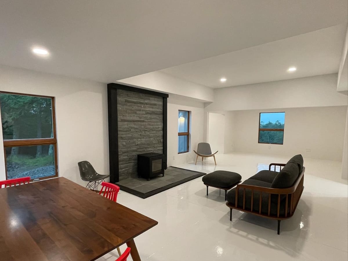 Wide-angle view of a spacious living room with minimalistic furniture, featuring a dark stone fireplace and modern décor in a newly built home in Catskill.