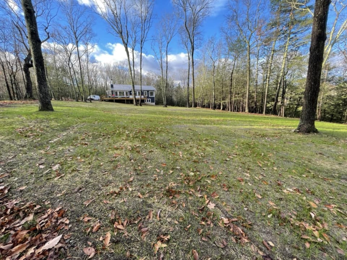 A large grassy field with a house in the background, surrounded by trees, showcasing a cleared lot for residential development.