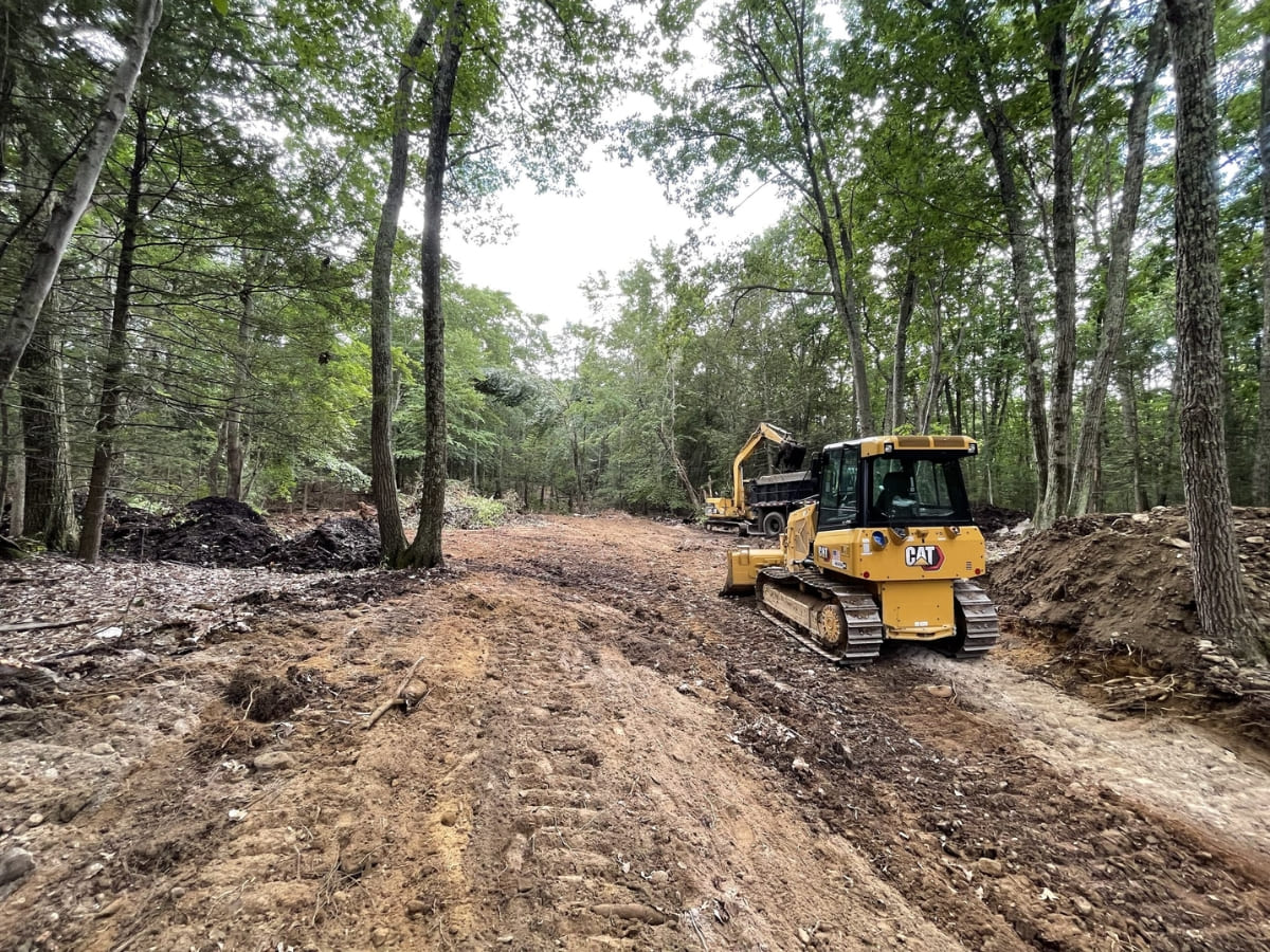 Excavation equipment working in a wooded area, preparing the ground for construction or landscaping as part of a large-scale project.