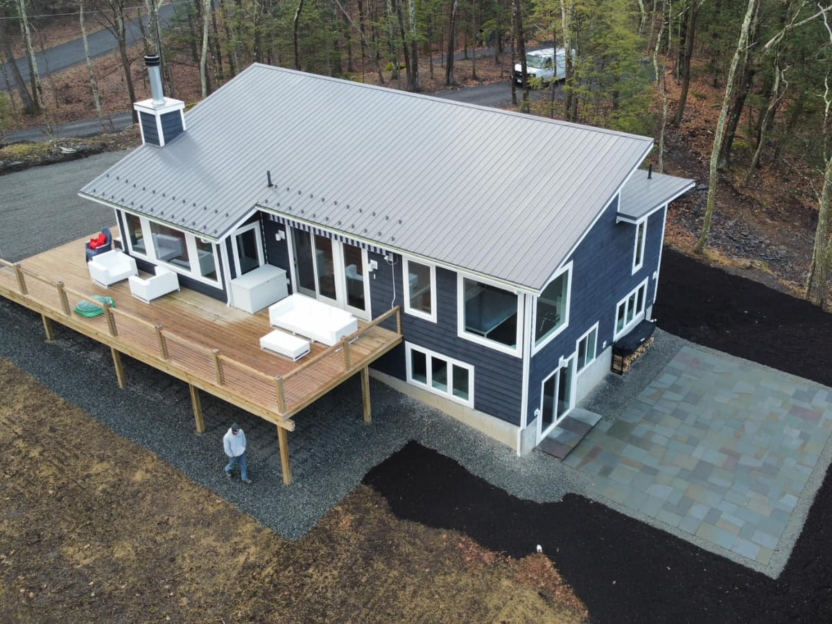 A modern home with a large wooden deck, stone patio, and newly landscaped surrounding area with mulch and gravel.