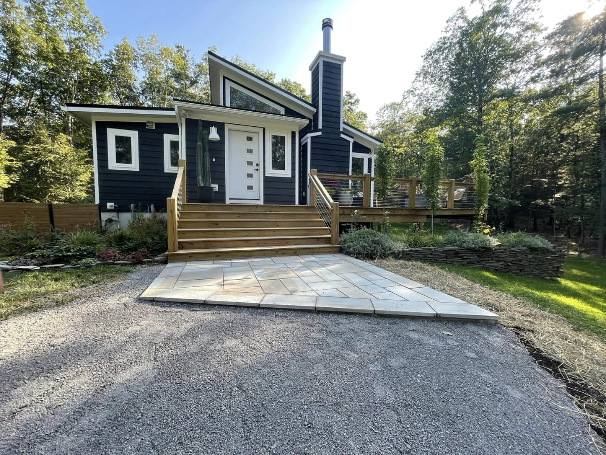 Front view of a modern house with a newly installed stone pathway leading up to the wooden front deck, framed by landscaped greenery and a gravel driveway.