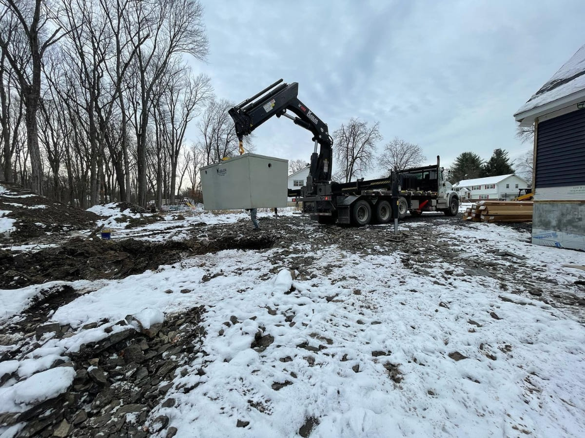 Heavy equipment lifting materials on a snowy construction site, working on a septic system installation for a residential project.