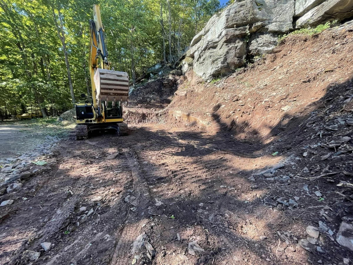 Excavation work on a rocky slope with heavy machinery clearing the area for development or landscaping purposes.