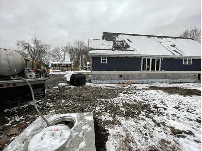 Excavation machinery in operation, installing a large septic system in a residential backyard covered in snow, with a truck and house in the background.