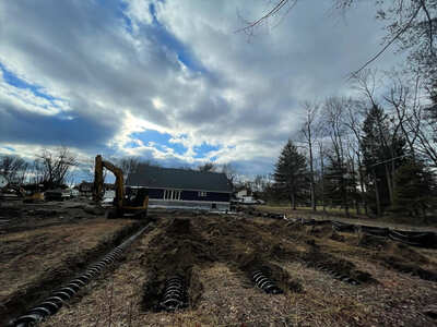 Excavator working on the installation of a septic system on a large open plot of land in Athens, with drainage trenches visible in the foreground.