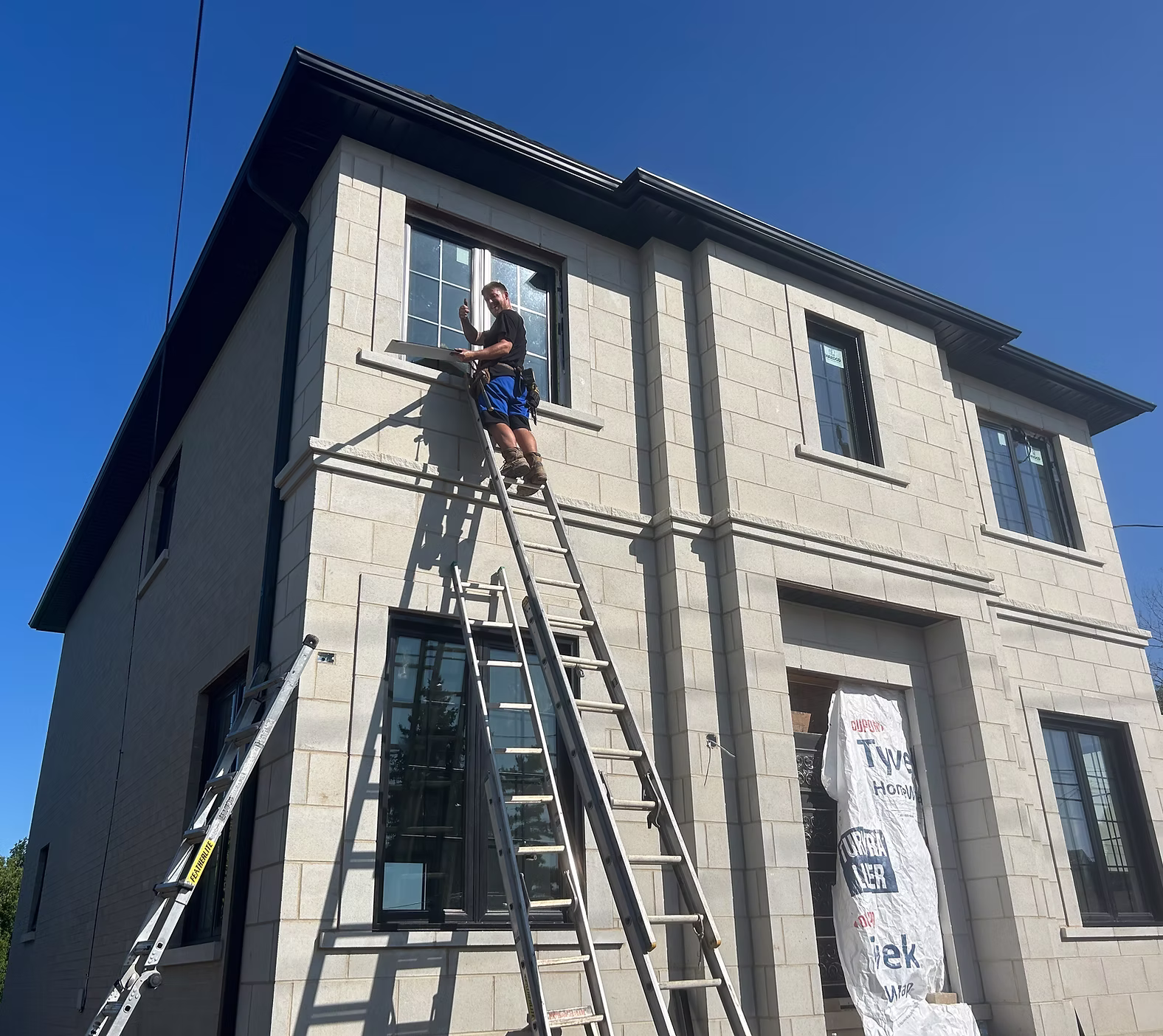 Infinity Gutters crew installing black seamless gutters and downspouts on a modern residential home exterior in Toronto, Ontario
