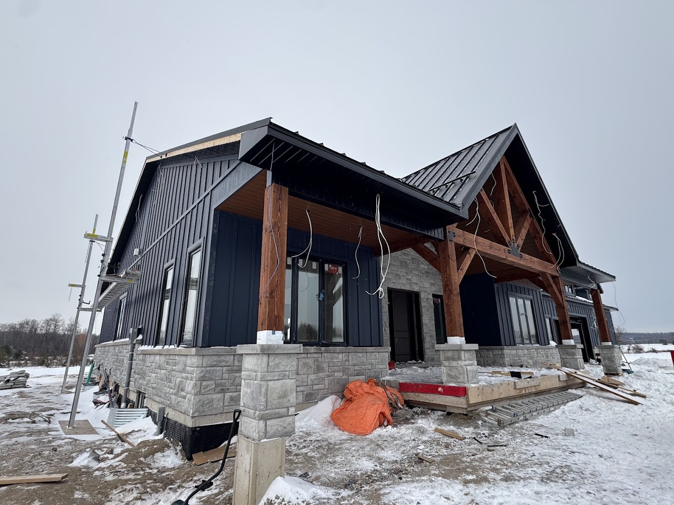 Custom Hamilton-area home with black vertical siding, standing seam metal roofing, timber beams, and stone exterior finishes