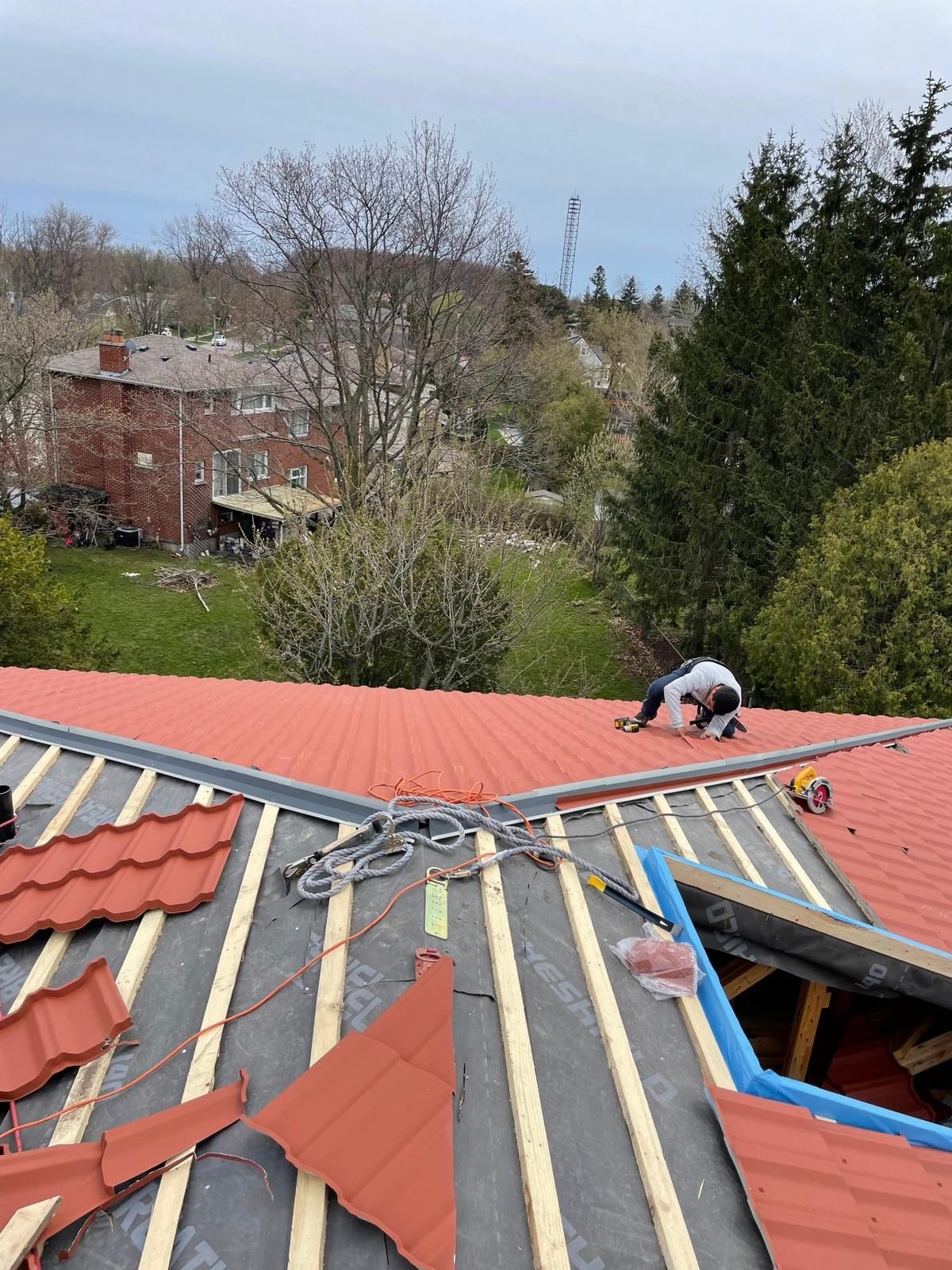 Roofing contractor installing red metal roof panels on a Hamilton-area home