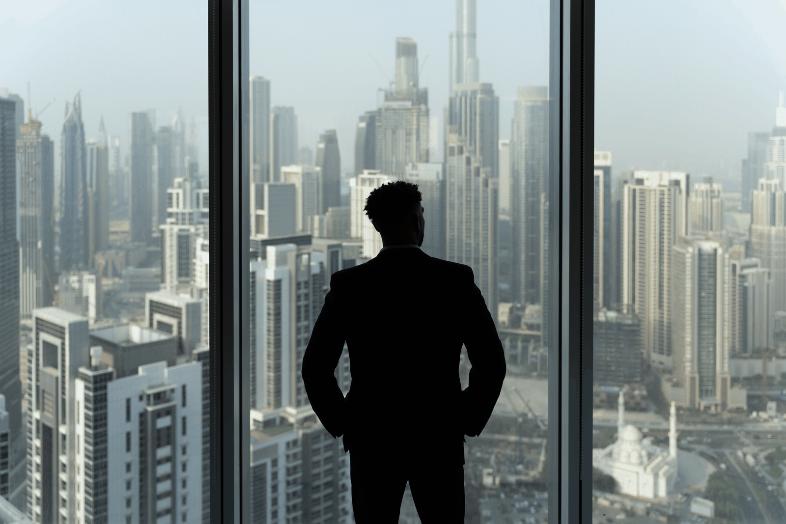 A man in a suit looking out over the Dubai skyline from an office window