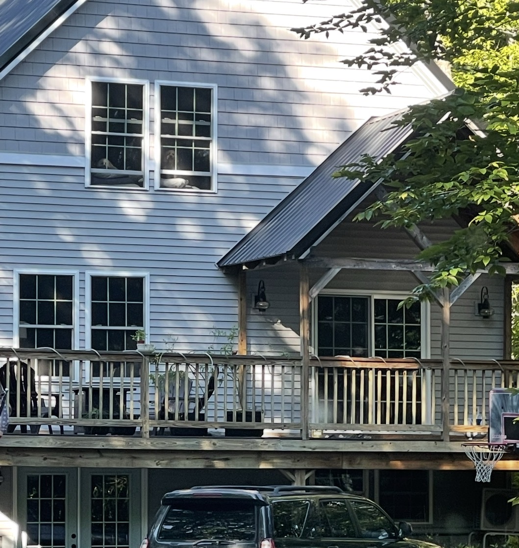 Exterior property work — grey house with deck and metal roof