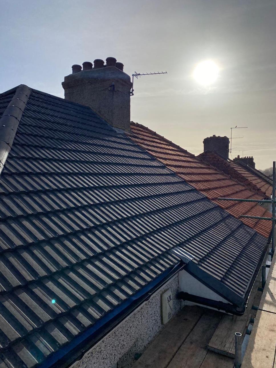 Finished dark tiled roof beside an older red roof