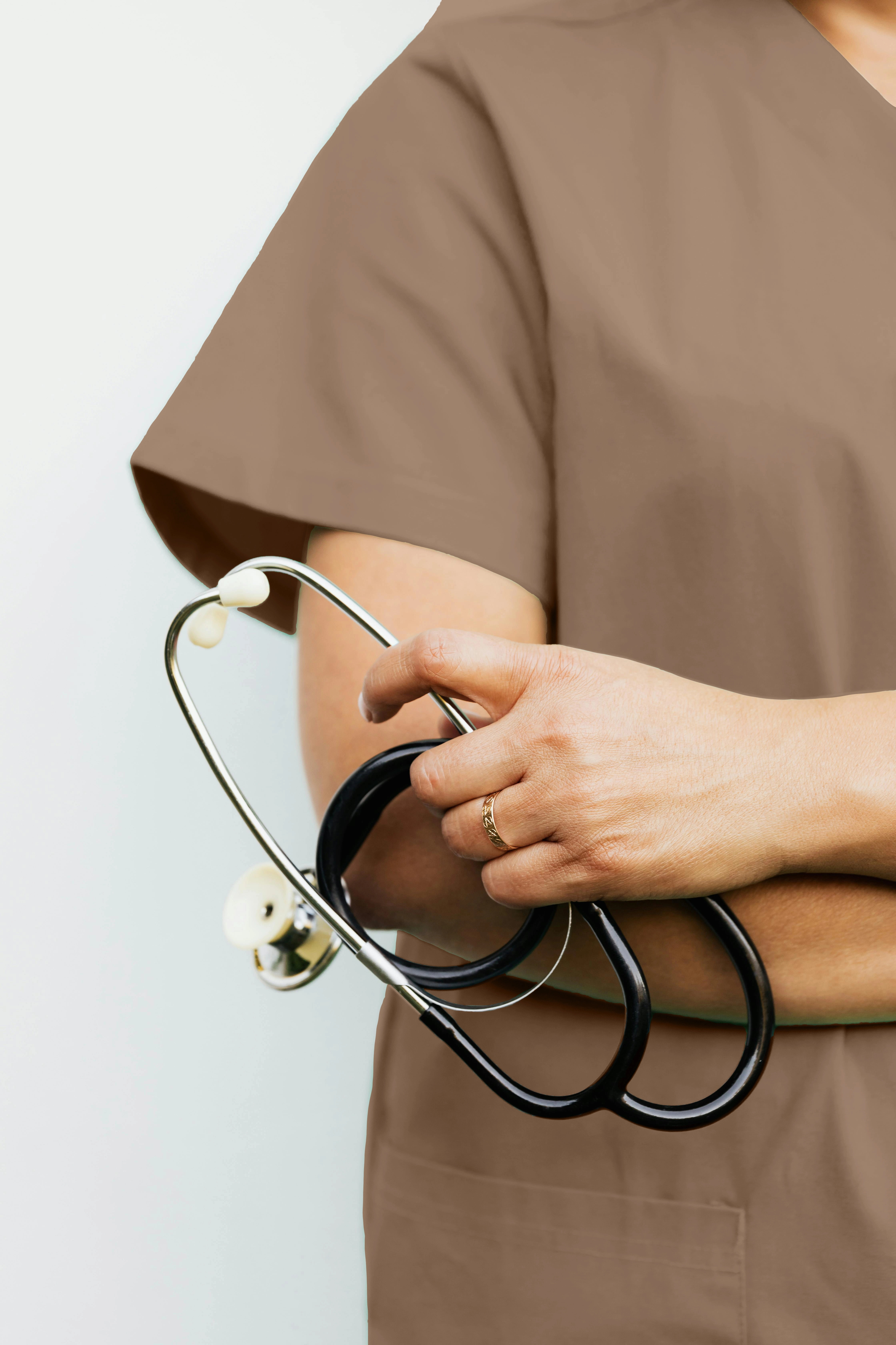 Close-up of a nurse's hand holding a stethoscope, showcasing a gold ring on her finger.