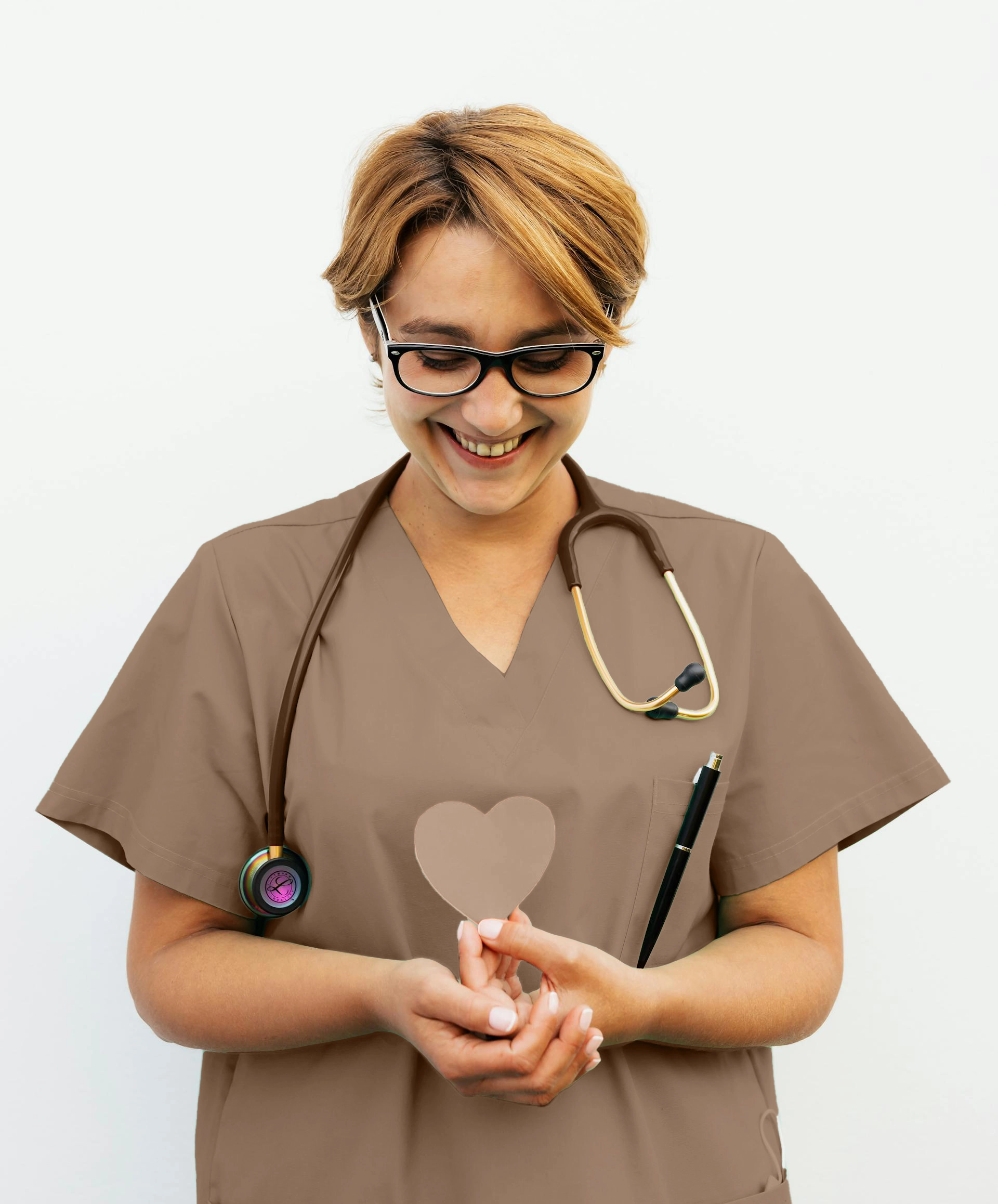 Female nurse in scrubs holding a heart-shaped object, smiling and standing against a plain white background.