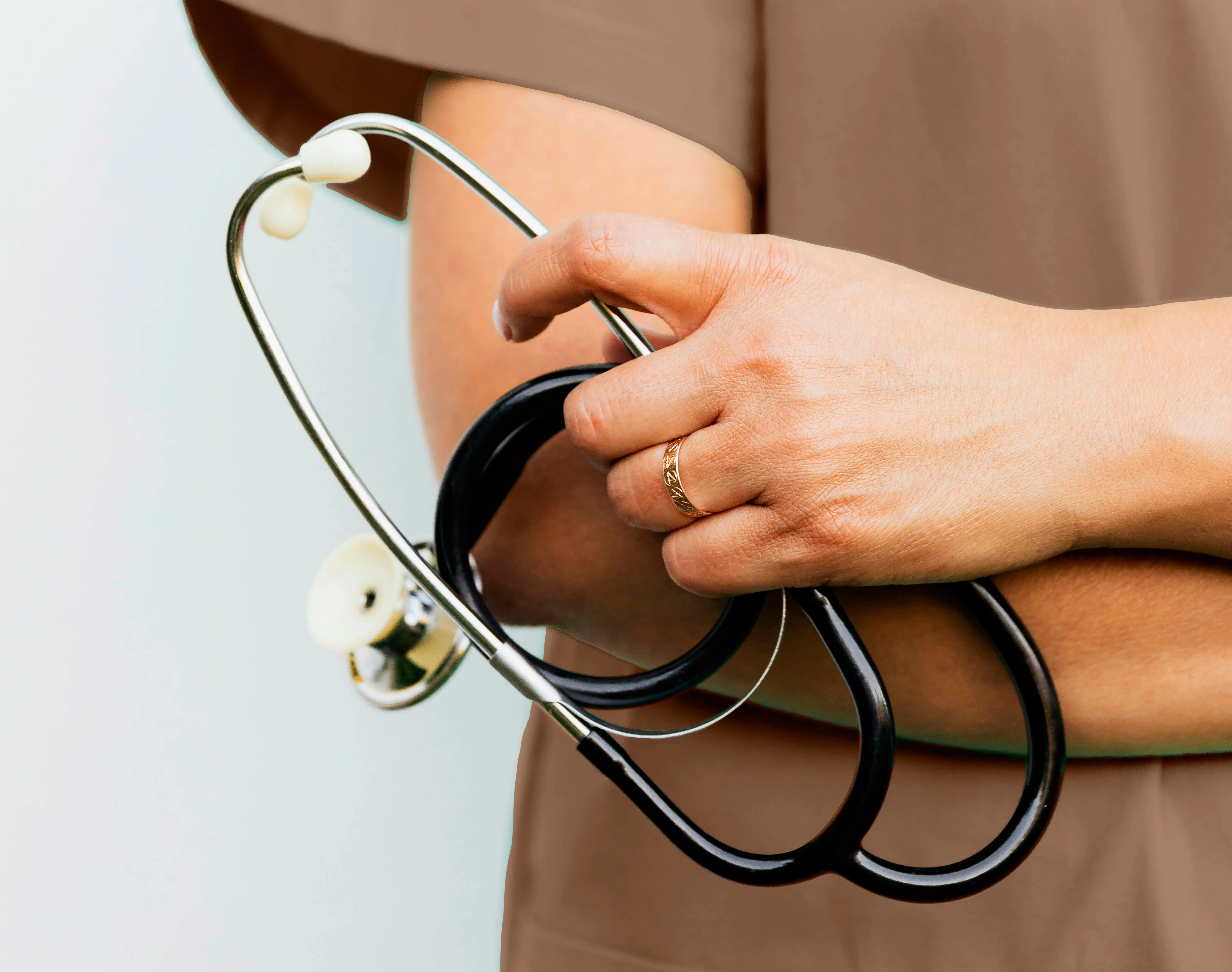 Close-up of a nurse's hand holding a stethoscope, showcasing a gold ring on her finger.