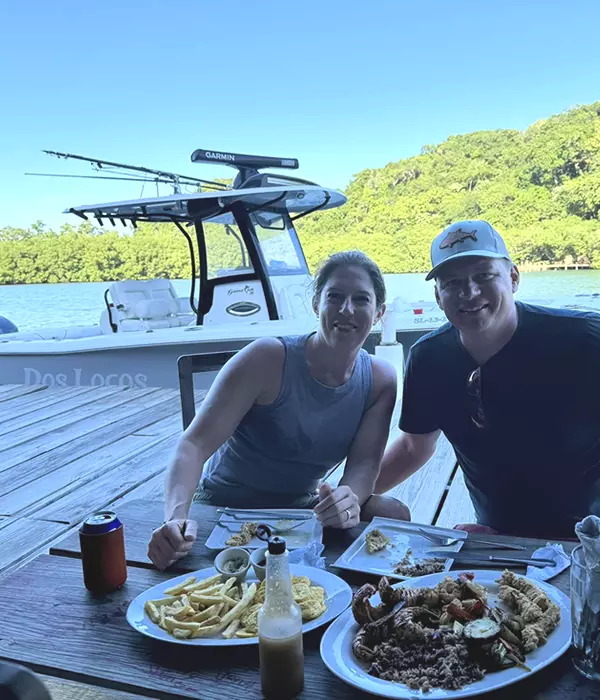 man and woman enjoying a fried seafood with boat in background