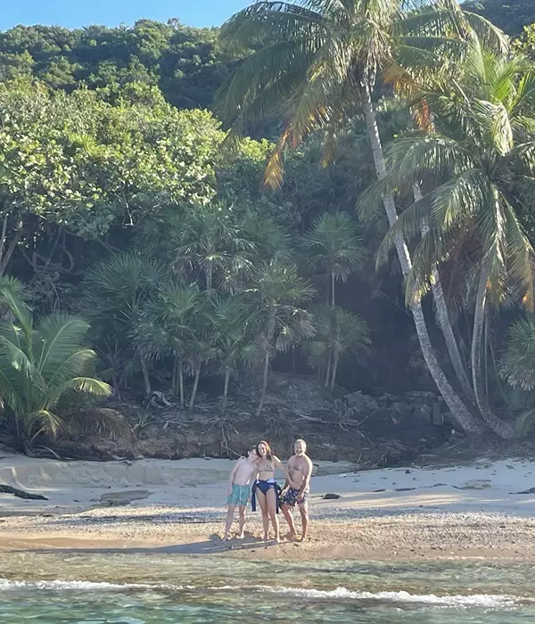 family standing on a beach with palmtrees and forest in background