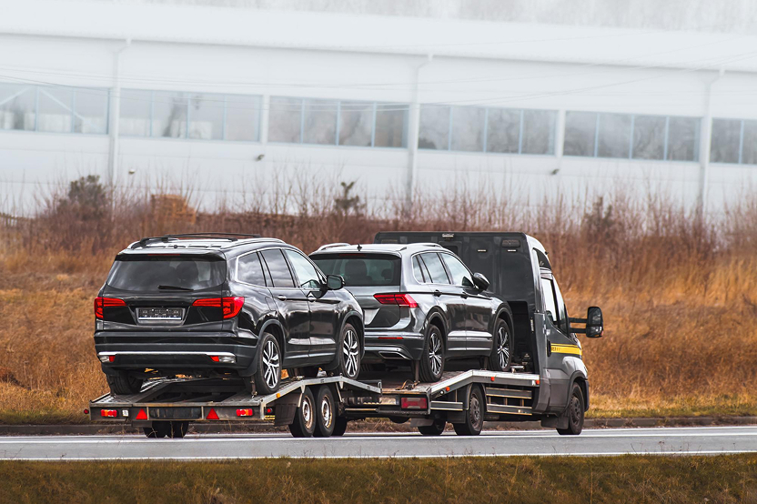 Two black SUVs loaded on a flatbed auto transport carrier on a road