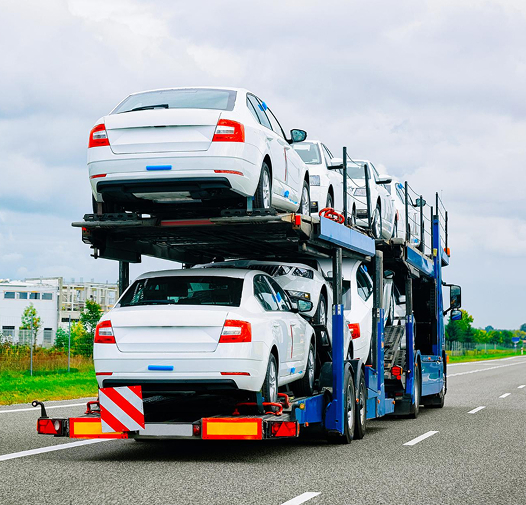 Open auto transport carrier hauling multiple white vehicles on a highway