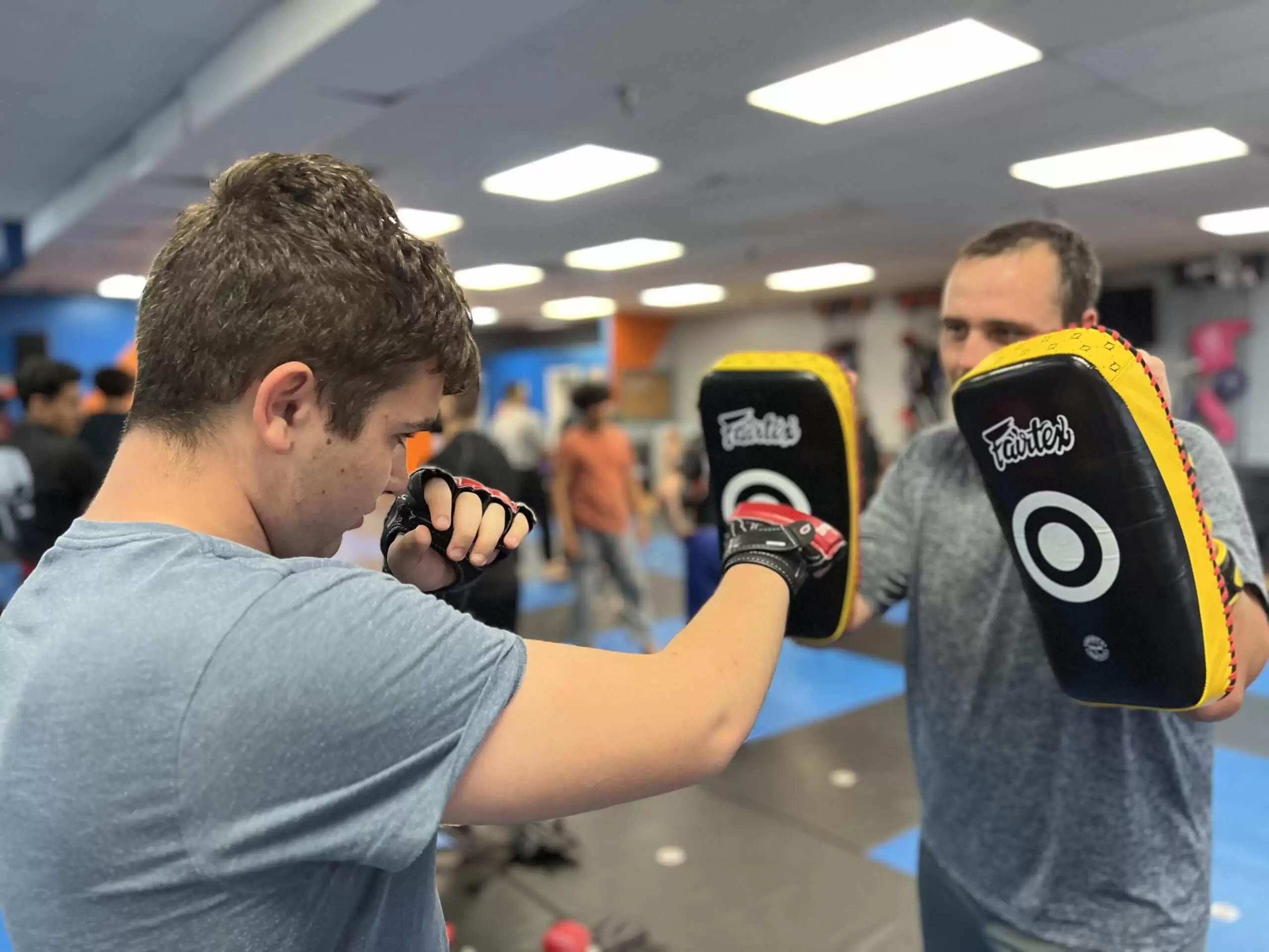 Adult kickboxing class in Fresno at Ultimate Martial Arts, student striking focus mitts held by a coach