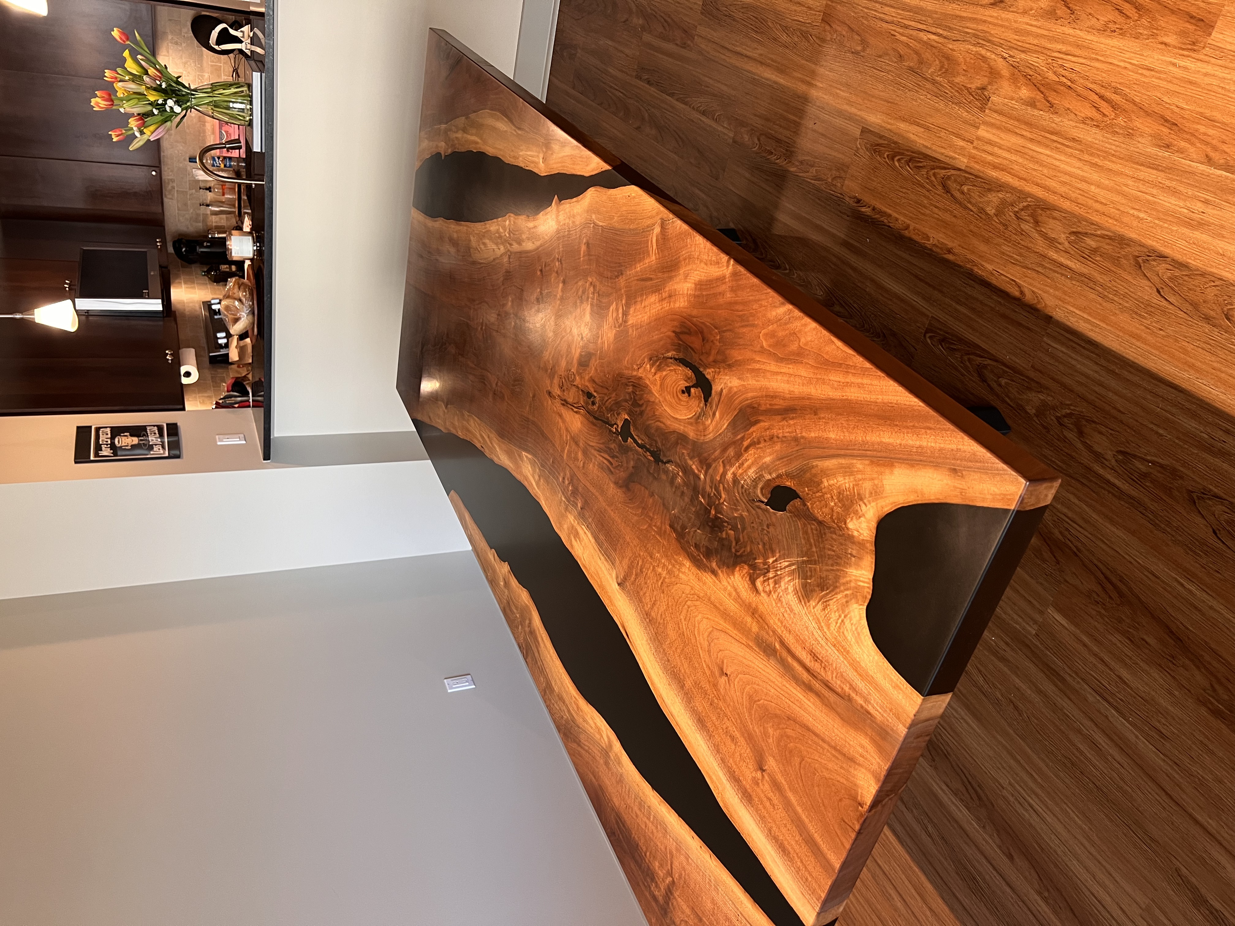 A custom live-edge wooden dining table joined by a black epoxy resin river, seen from above in a modern room.