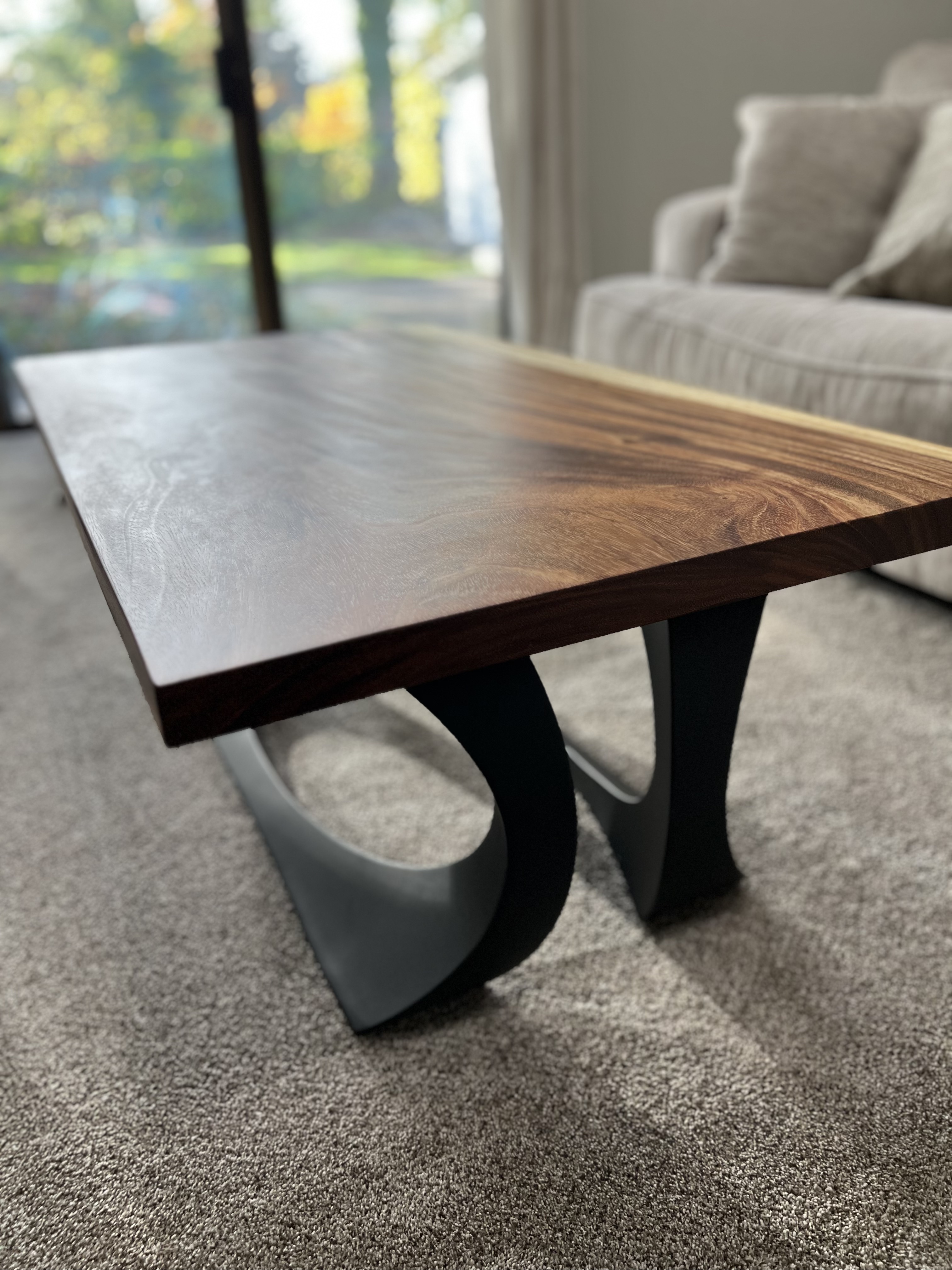 A modern coffee table with a dark live-edge top on curved matte black metal legs.