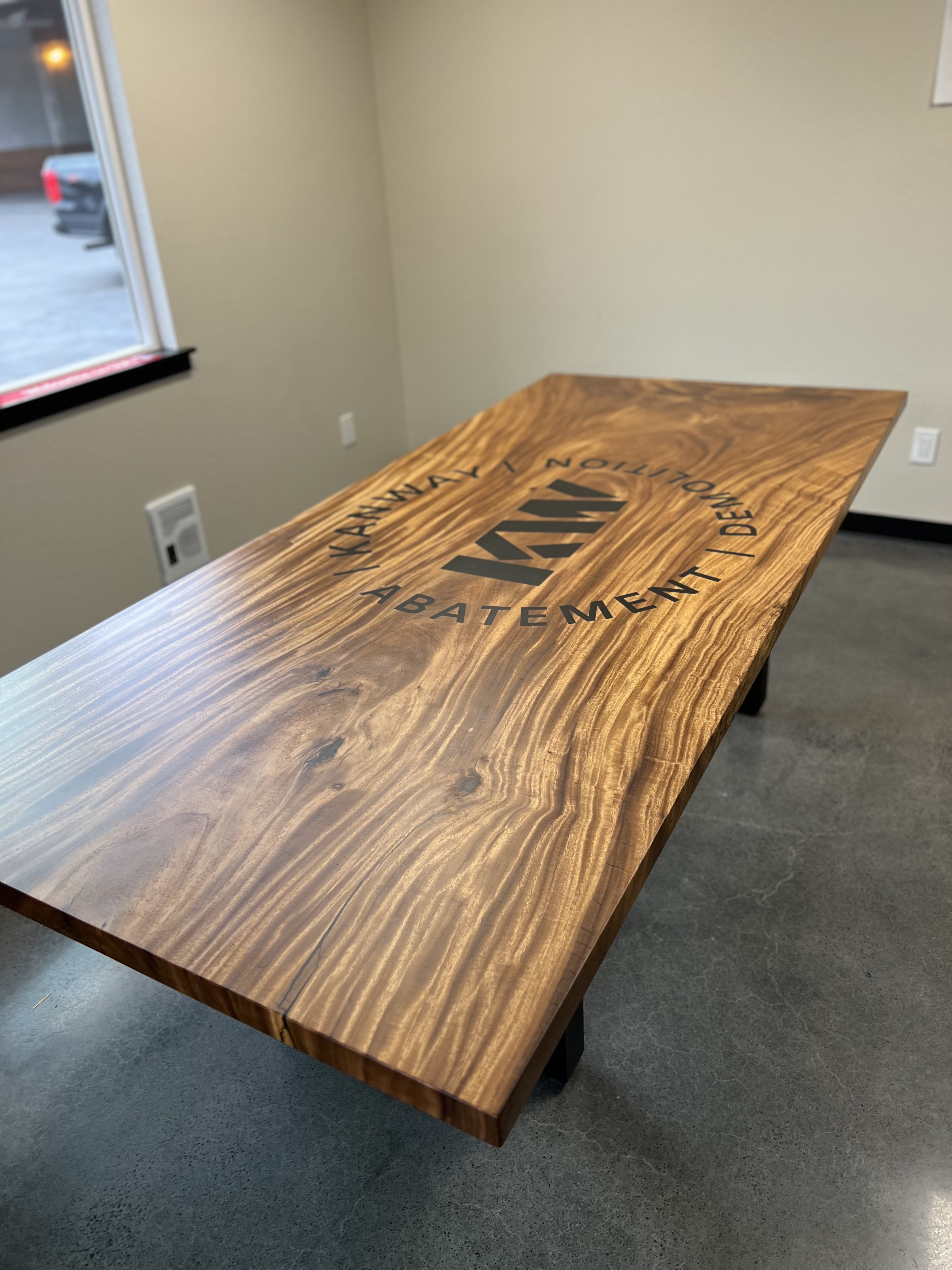A custom wooden conference table with a client logo inlaid at its centre, in a minimalist office.