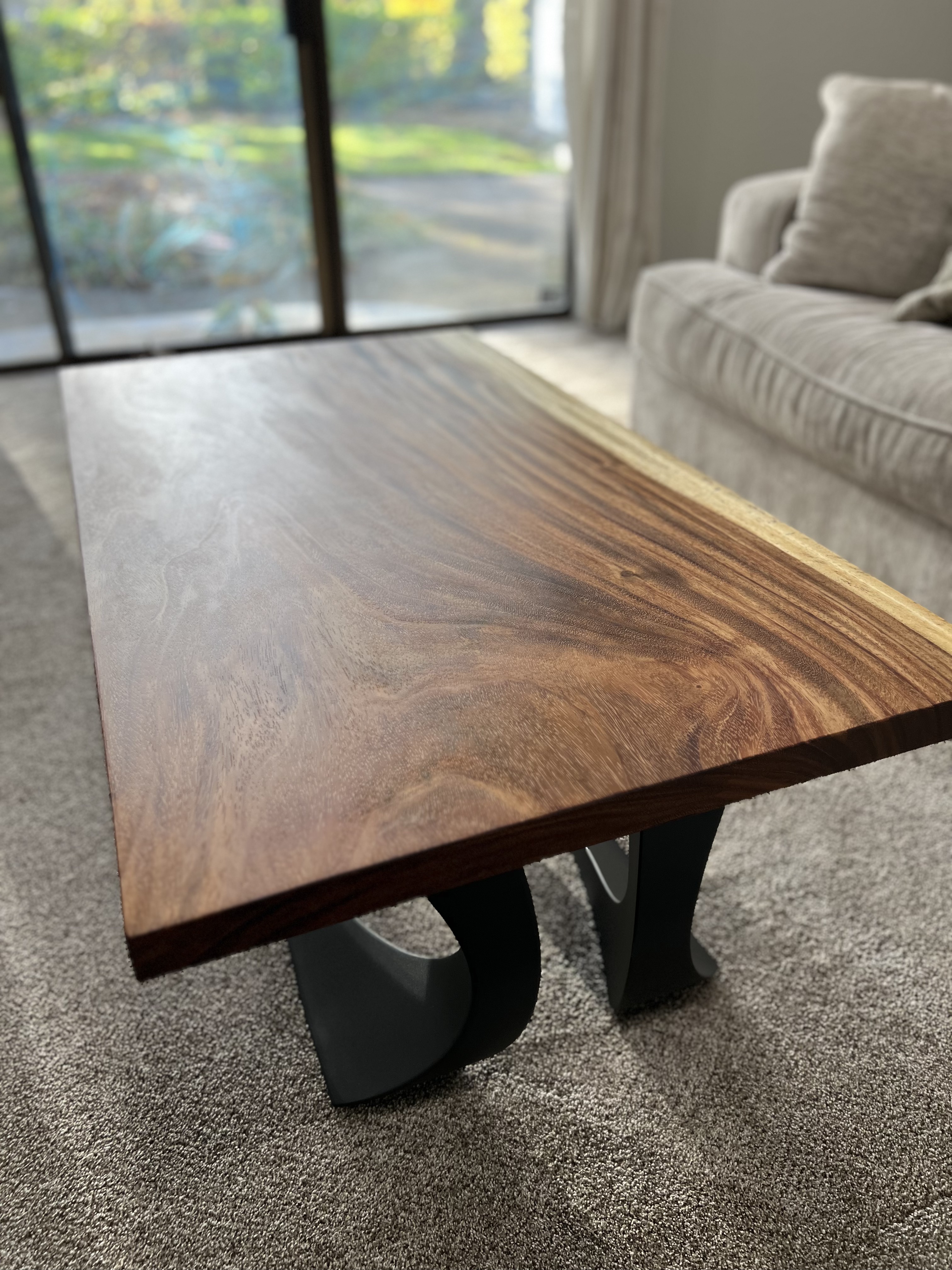 A live-edge wood coffee table with curved black metal legs in a sunlit living room.