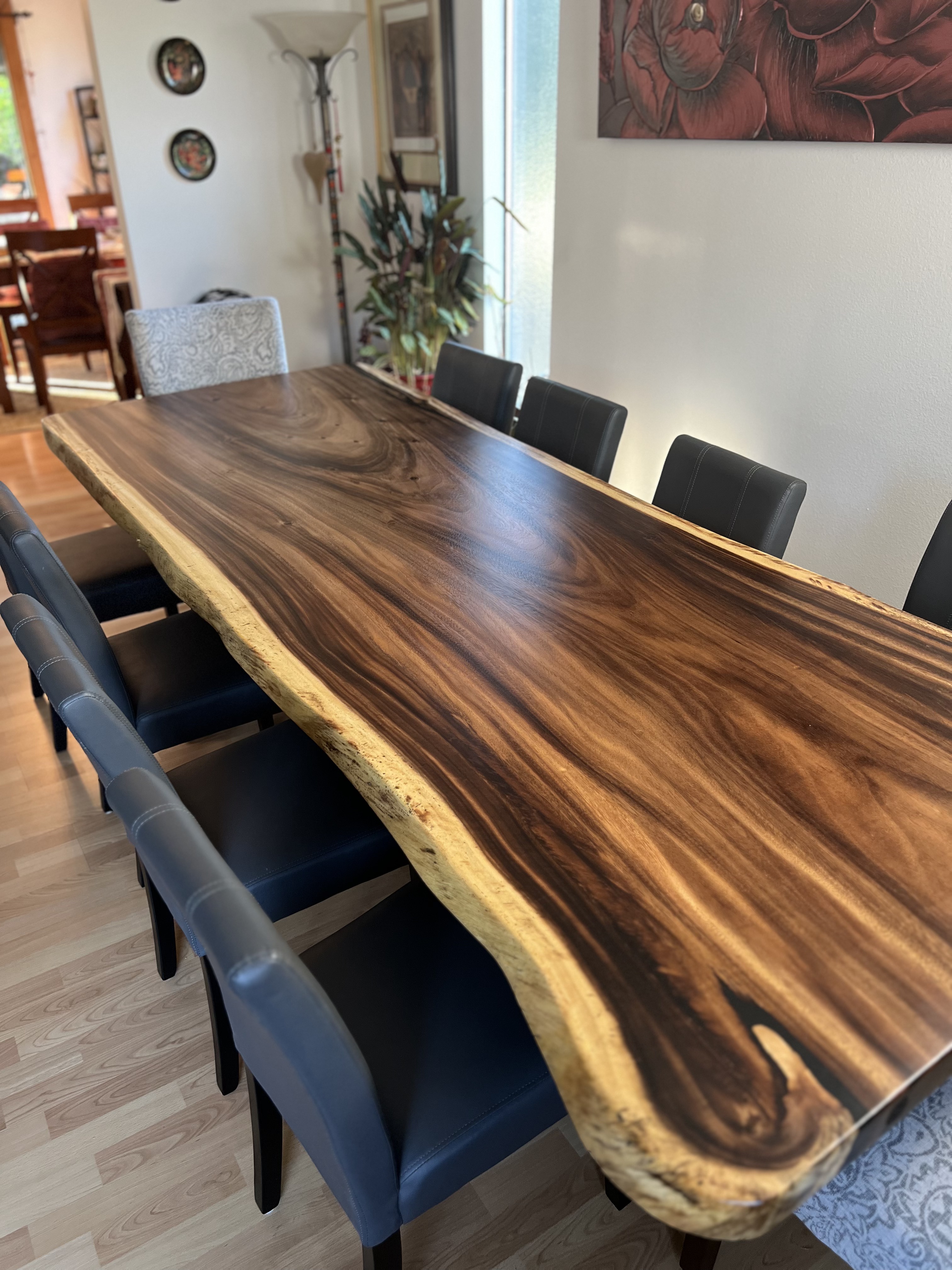 A long dark-wood live-edge dining table surrounded by grey upholstered chairs in a bright dining room.