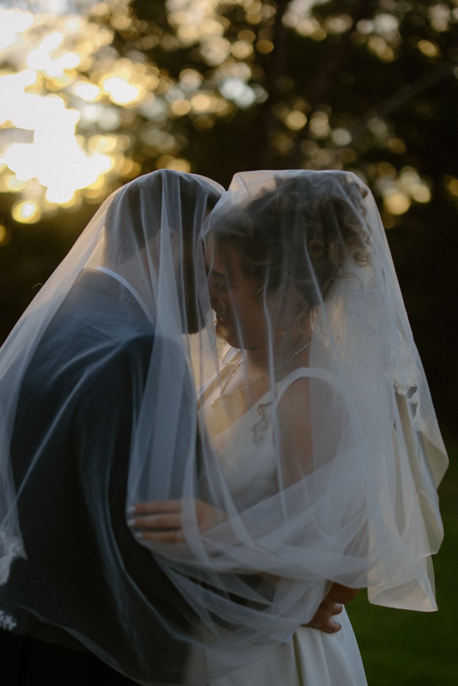 Couple close together beneath a veil in late afternoon light