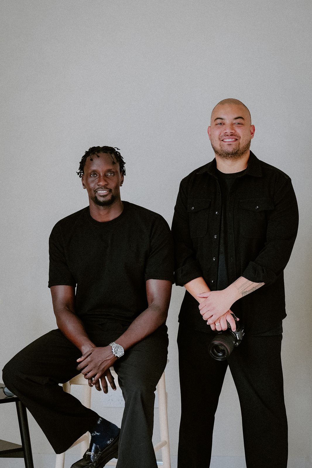 Two of the By Hidden Leaf crew photographed together in the studio, one holding a camera