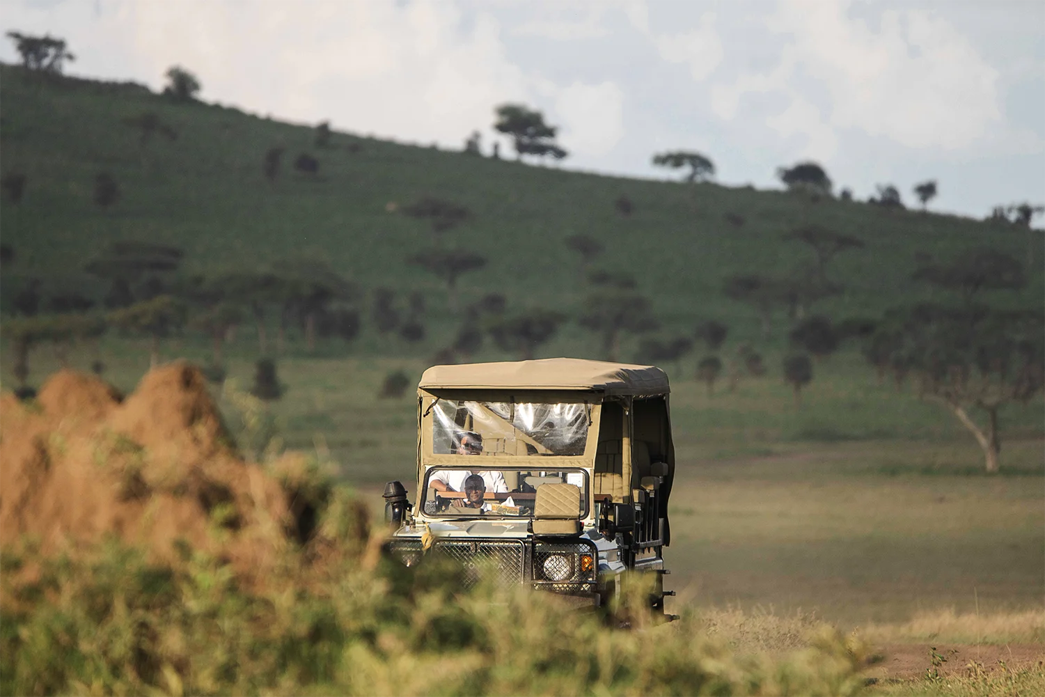 A safari vehicle moving through green Serengeti hills