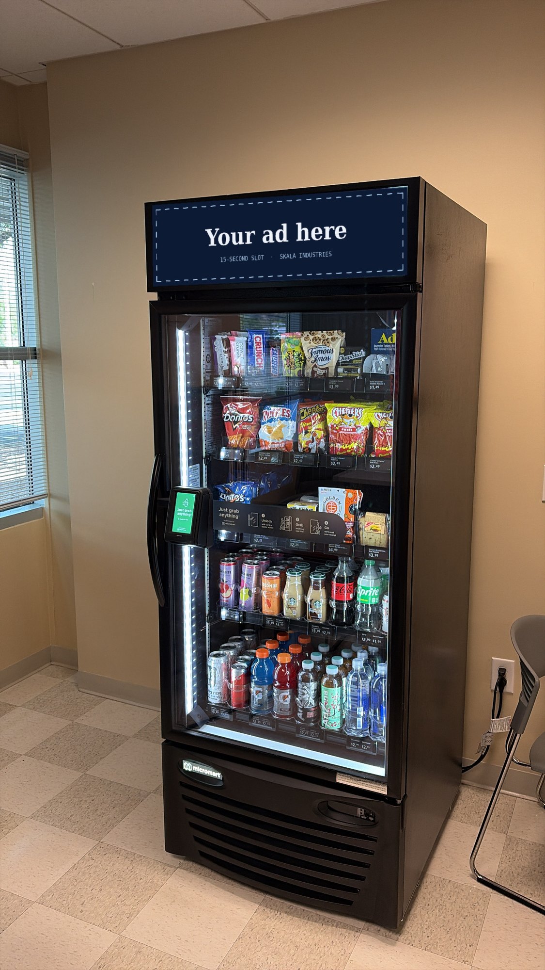 An AI smart cooler in a staff break room, with &ldquo;Your ad here&rdquo; on the digital screen above the door.