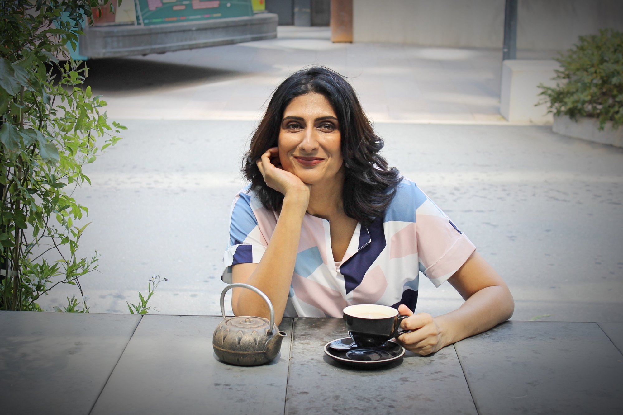 Salena Kulkarni at an outdoor café table with a coffee, smiling