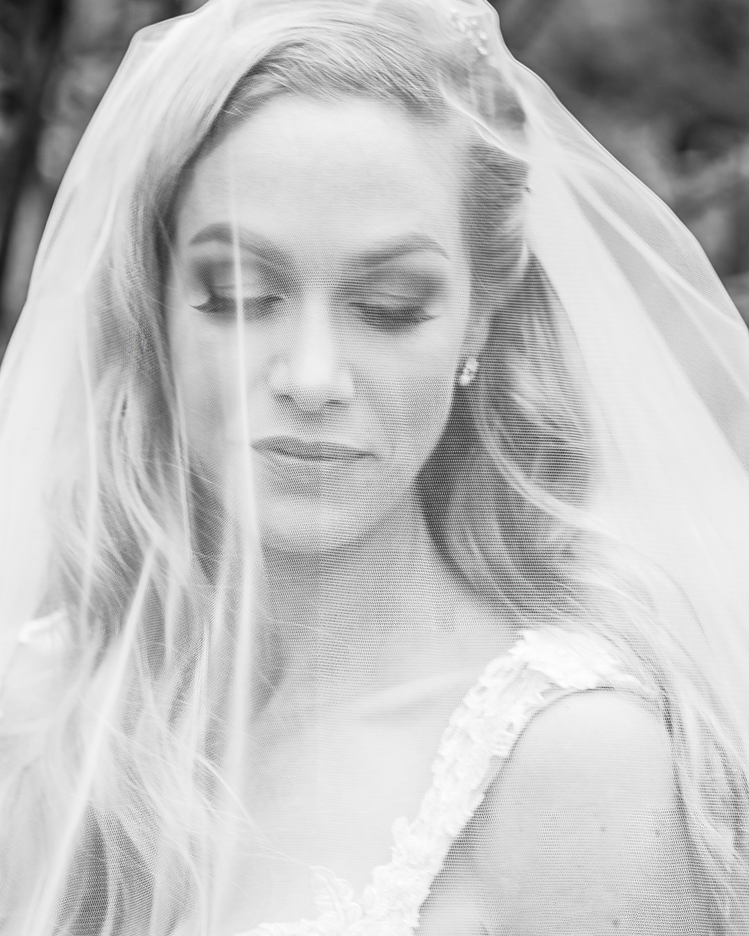 A Seattle bride is under a cathedral length veil looking down. The photo is in black and white. The bride's handmade floral bridal gown is white. 