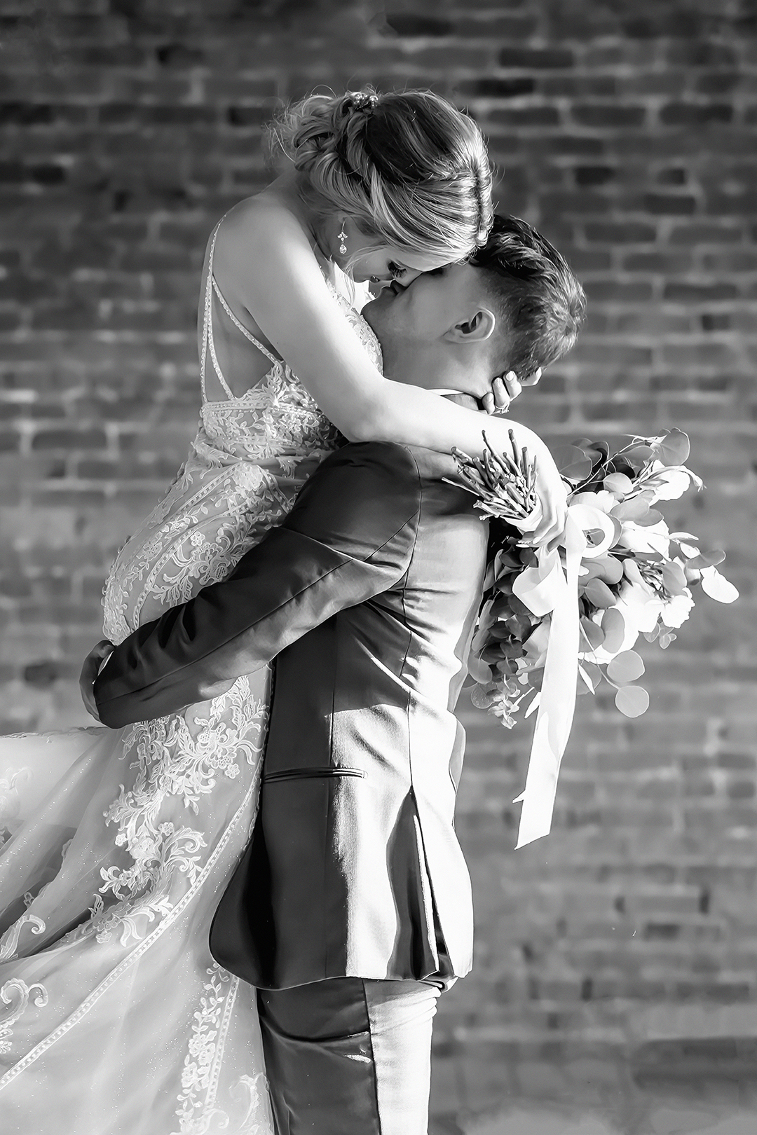 Bridal couple kissing. Man lifts woman in his arms while they kiss. 